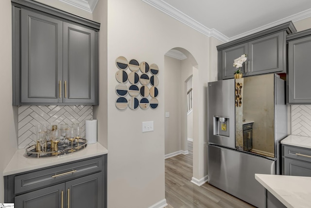 kitchen with decorative backsplash, light wood-type flooring, crown molding, stainless steel fridge with ice dispenser, and gray cabinets