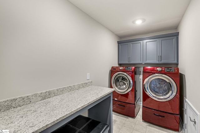 clothes washing area featuring washer and dryer, light tile patterned flooring, and cabinets