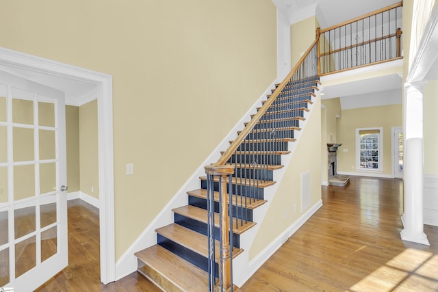 stairway featuring wood-type flooring, a towering ceiling, and decorative columns