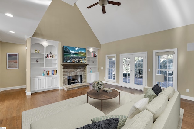 living room featuring built in shelves, french doors, a stone fireplace, high vaulted ceiling, and wood-type flooring