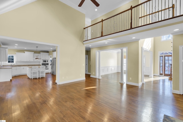 unfurnished living room with hardwood / wood-style flooring, ceiling fan, a towering ceiling, ornamental molding, and ornate columns