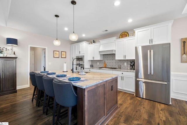 kitchen featuring dark hardwood / wood-style floors, an island with sink, appliances with stainless steel finishes, decorative light fixtures, and white cabinetry