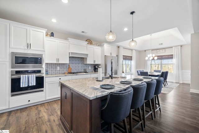 kitchen featuring an island with sink, white cabinets, stainless steel appliances, and decorative light fixtures