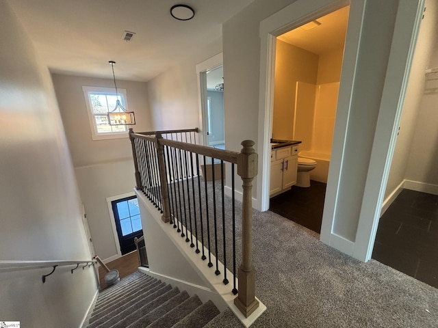 stairs with carpet floors and an inviting chandelier