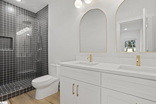 bathroom with hardwood / wood-style floors, vanity, toilet, and a tile shower