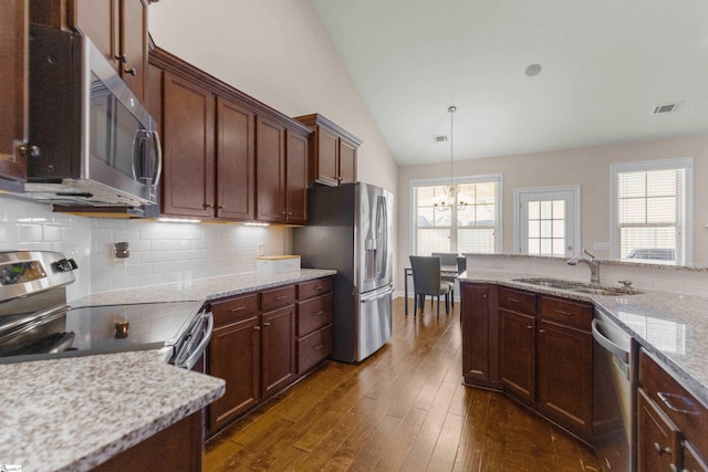 kitchen with pendant lighting, lofted ceiling, light stone countertops, appliances with stainless steel finishes, and a notable chandelier