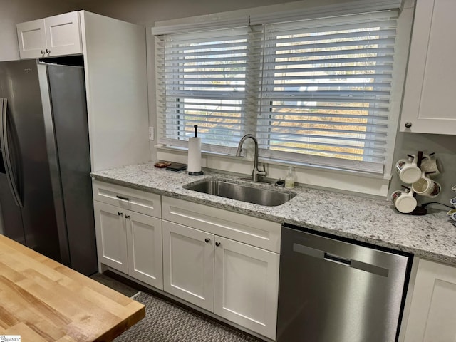 kitchen with white cabinetry, sink, light stone countertops, and appliances with stainless steel finishes