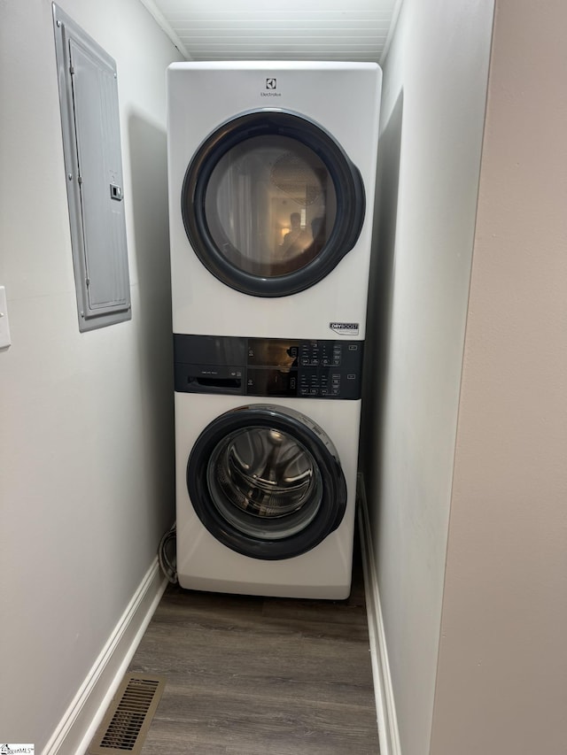 clothes washing area featuring electric panel, stacked washing maching and dryer, and hardwood / wood-style flooring