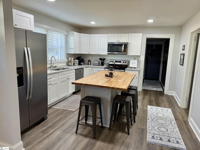 kitchen with butcher block counters, white cabinetry, sink, stainless steel appliances, and a kitchen island