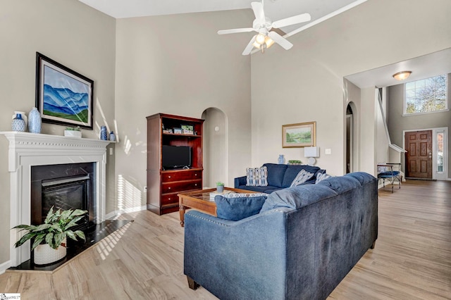 living room with ceiling fan, a towering ceiling, and light wood-type flooring