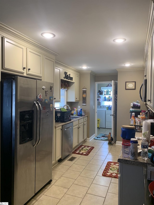 kitchen with washer and dryer, light tile patterned floors, appliances with stainless steel finishes, and cream cabinets