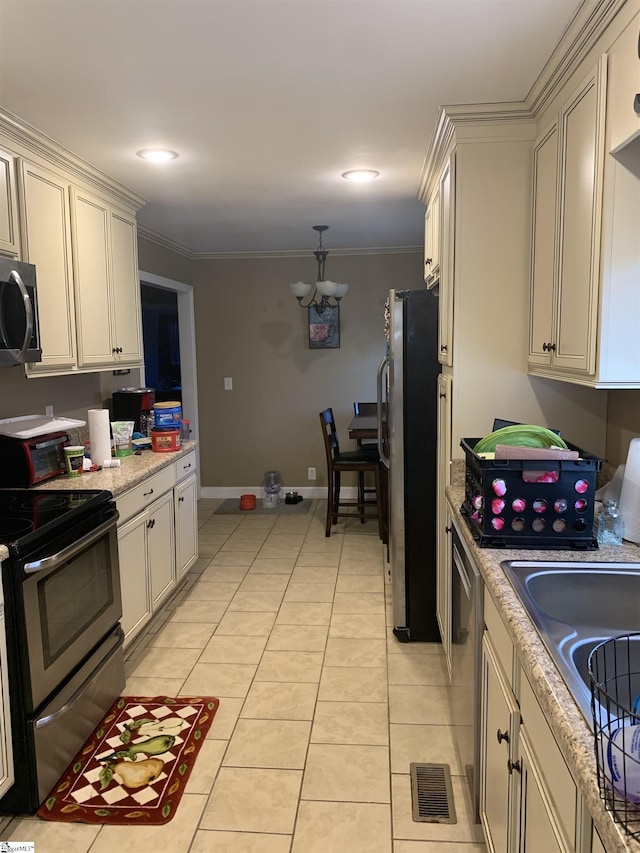 kitchen featuring stainless steel appliances, cream cabinets, a chandelier, light tile patterned flooring, and ornamental molding