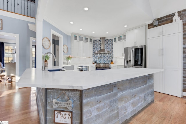 kitchen featuring appliances with stainless steel finishes, backsplash, sink, wall chimney range hood, and white cabinets