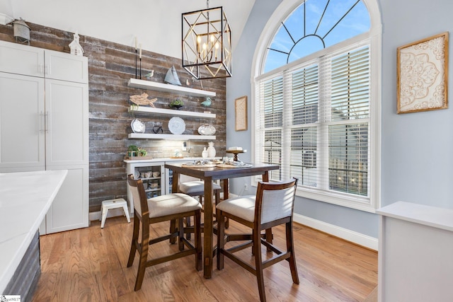 dining area with light hardwood / wood-style floors, an inviting chandelier, a wealth of natural light, and wood walls