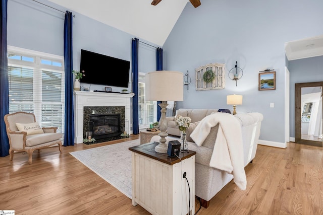 living room with high vaulted ceiling, ceiling fan, a high end fireplace, and light hardwood / wood-style flooring