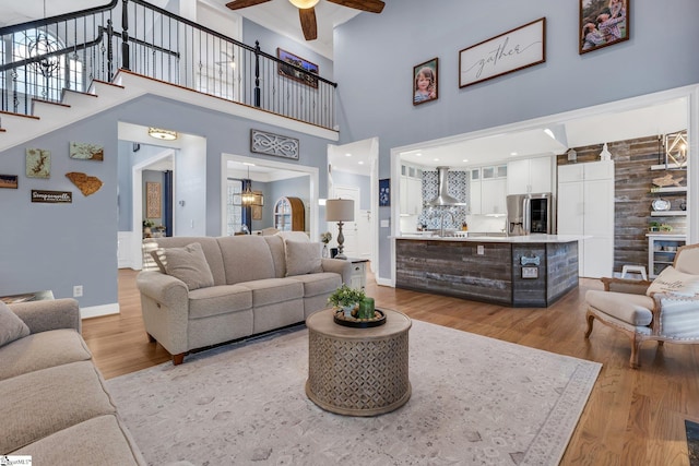 living room featuring sink, light hardwood / wood-style flooring, ceiling fan, a towering ceiling, and beam ceiling