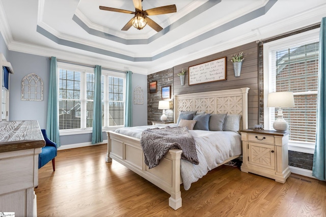 bedroom with a tray ceiling, ceiling fan, crown molding, and light hardwood / wood-style floors