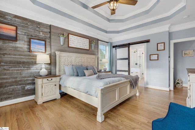 bedroom featuring a tray ceiling, a barn door, wooden walls, and ceiling fan