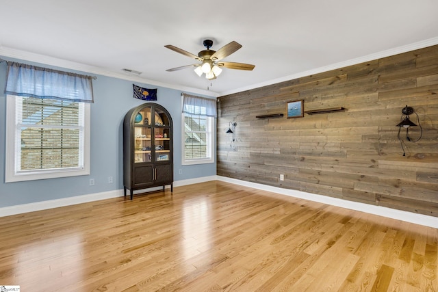 unfurnished room with ceiling fan, wood walls, crown molding, and light hardwood / wood-style flooring