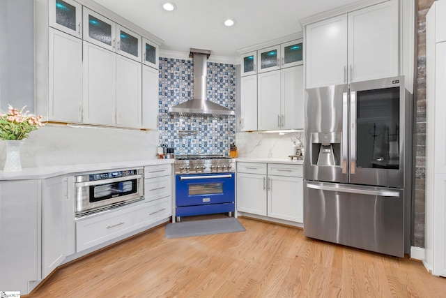 kitchen with white cabinets, wall chimney exhaust hood, decorative backsplash, and stainless steel appliances