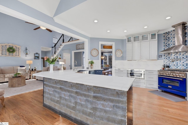 kitchen with decorative backsplash, high end stainless steel range oven, wall chimney range hood, light hardwood / wood-style floors, and white cabinetry