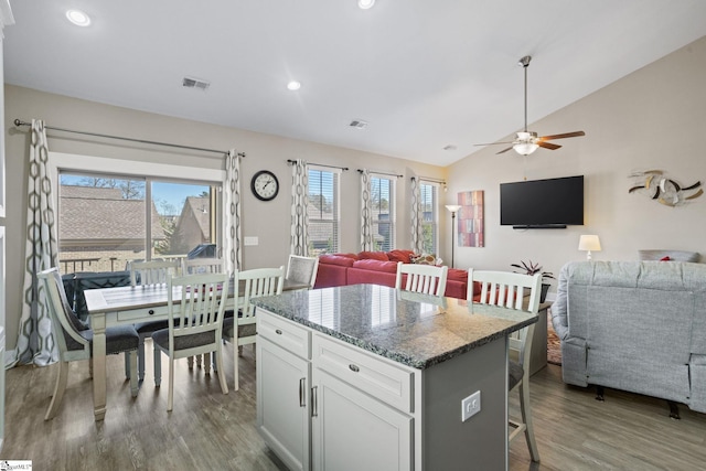 kitchen with white cabinetry, a center island, a kitchen breakfast bar, dark stone countertops, and wood-type flooring