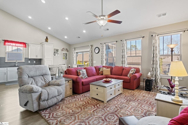 living room with light wood-type flooring, vaulted ceiling, ceiling fan, and sink