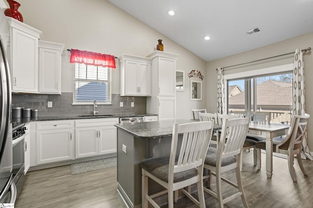 kitchen with dark stone counters, a healthy amount of sunlight, sink, white cabinets, and lofted ceiling