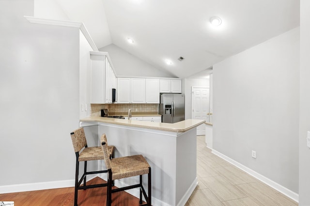 kitchen with kitchen peninsula, stainless steel refrigerator with ice dispenser, a kitchen breakfast bar, white cabinets, and lofted ceiling