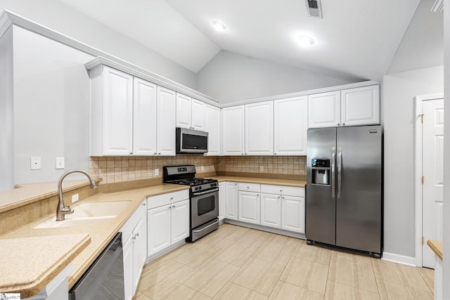 kitchen with white cabinetry, sink, stainless steel appliances, vaulted ceiling, and decorative backsplash