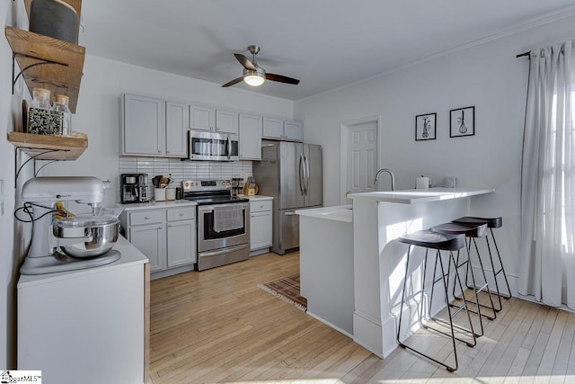 kitchen with ceiling fan, decorative backsplash, appliances with stainless steel finishes, light hardwood / wood-style floors, and a kitchen bar