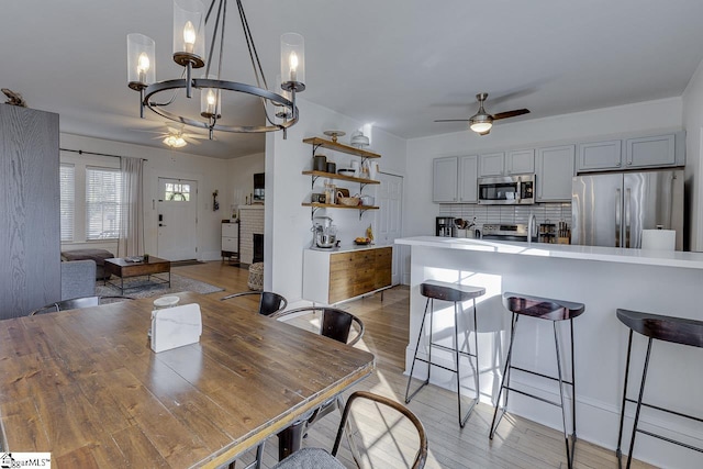 dining room with ceiling fan with notable chandelier and light wood-type flooring