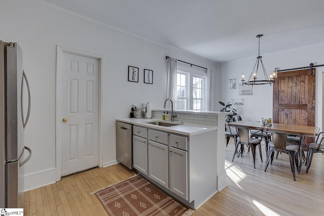 kitchen with stainless steel appliances, sink, a barn door, decorative light fixtures, and light hardwood / wood-style flooring