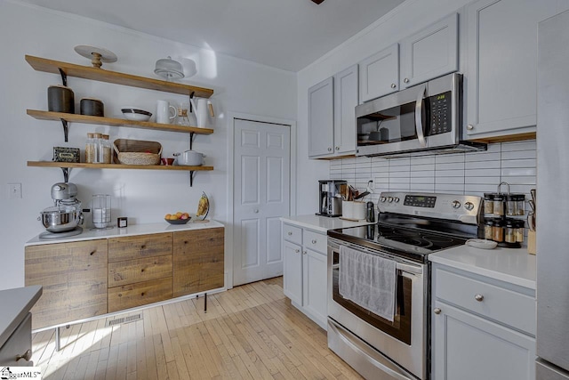 kitchen featuring backsplash, white cabinets, light hardwood / wood-style floors, and appliances with stainless steel finishes