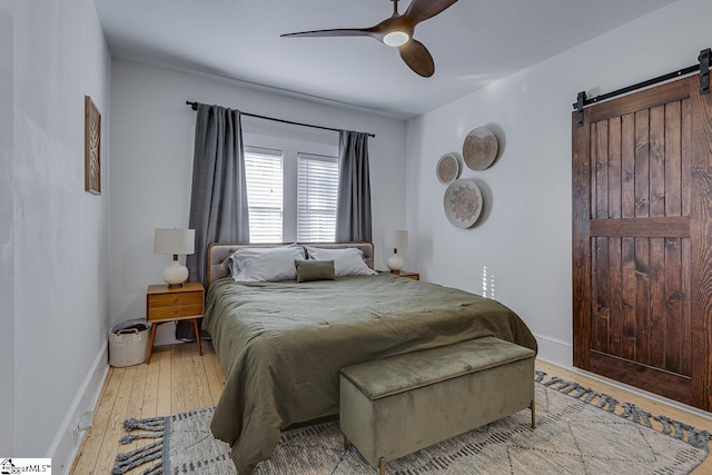 bedroom with light wood-type flooring, a barn door, and ceiling fan