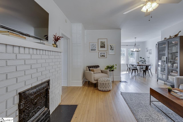 living room featuring a fireplace, light hardwood / wood-style flooring, and ceiling fan with notable chandelier