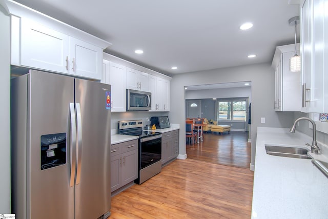 kitchen with white cabinetry, sink, light hardwood / wood-style floors, decorative light fixtures, and appliances with stainless steel finishes