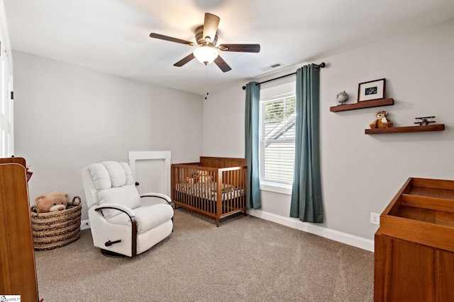 carpeted bedroom featuring ceiling fan and a nursery area