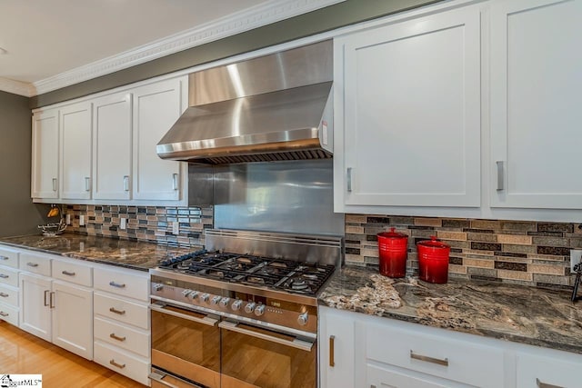 kitchen with high end stove, white cabinetry, dark stone counters, and wall chimney range hood