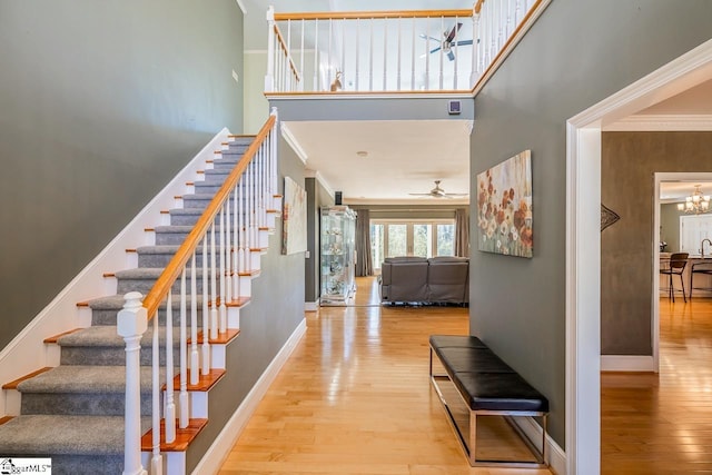 entryway featuring wood-type flooring, a high ceiling, baseboards, and ceiling fan with notable chandelier