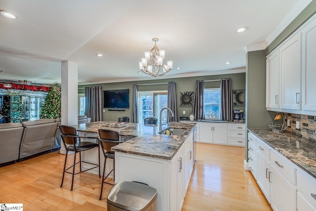 kitchen featuring backsplash, white cabinets, sink, and an island with sink