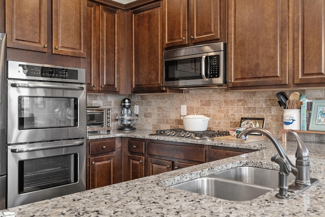 kitchen with tasteful backsplash, light stone countertops, sink, and stainless steel appliances