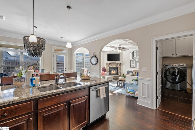 kitchen featuring a stone fireplace, sink, crown molding, stainless steel dishwasher, and decorative light fixtures