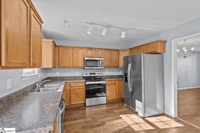 kitchen with sink, stainless steel appliances, a notable chandelier, wood-type flooring, and decorative light fixtures