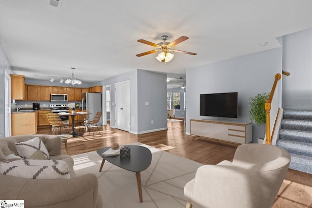 living room with sink, ceiling fan with notable chandelier, and light wood-type flooring