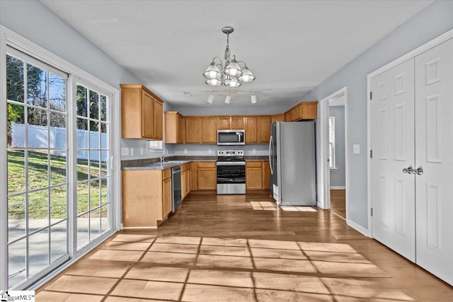 kitchen with appliances with stainless steel finishes, a healthy amount of sunlight, pendant lighting, and a notable chandelier