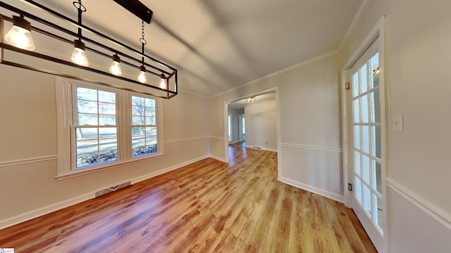 unfurnished dining area featuring vaulted ceiling, ornamental molding, and light hardwood / wood-style flooring