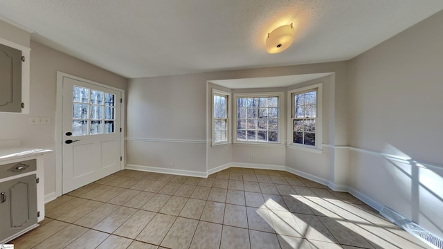 unfurnished dining area featuring a textured ceiling and light tile patterned flooring