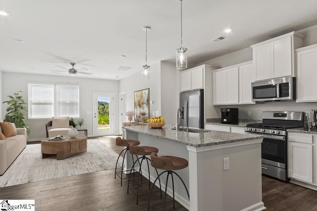 kitchen featuring hanging light fixtures, appliances with stainless steel finishes, white cabinetry, and a kitchen island with sink