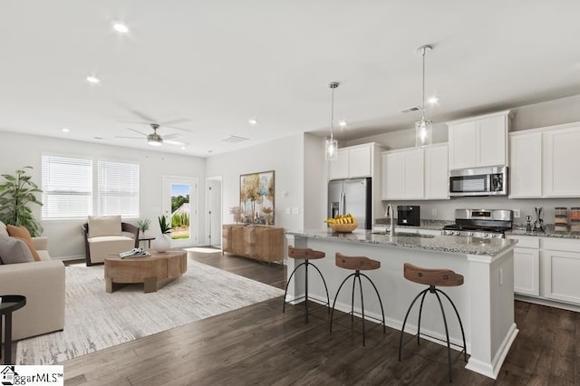 kitchen with white cabinets, appliances with stainless steel finishes, hanging light fixtures, and an island with sink